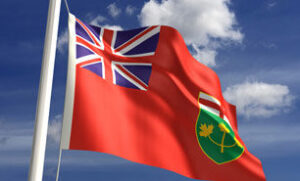 The Province of Ontario's flag blows in the wind against a backdrop of blue sky and white clouds.